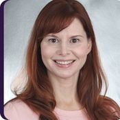 Fair skinned woman with long red hair in a pink shirt with grey background