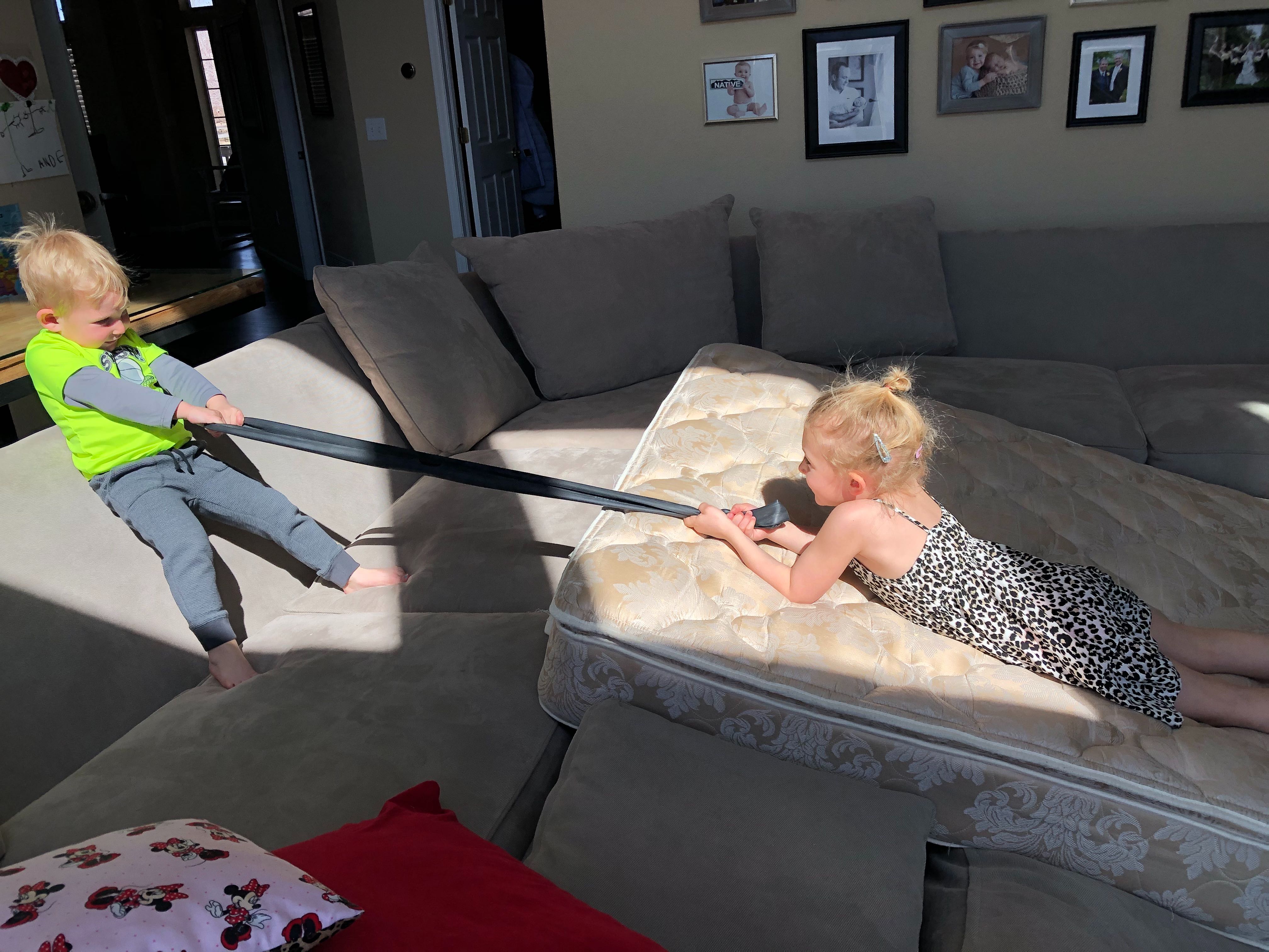 A boy pulls a young girl up a mattress mountain