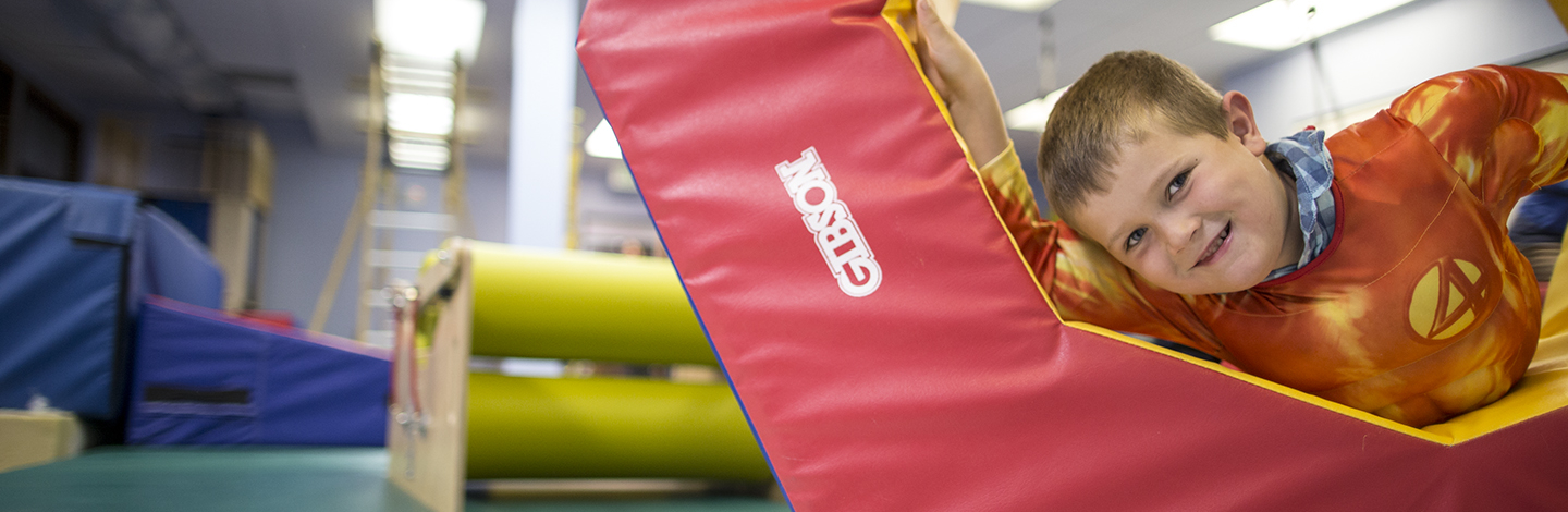 child in sensory gym laying on foam tumble block while looking at the camera and smiling