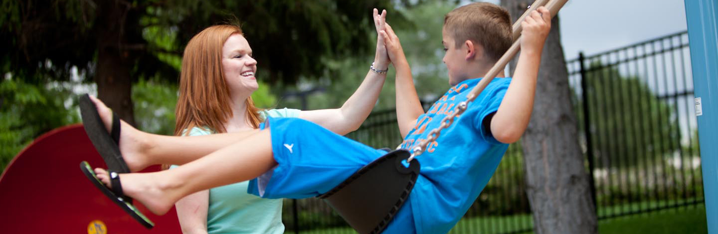 An Occupational Therapist gives a child in a swing a high five.