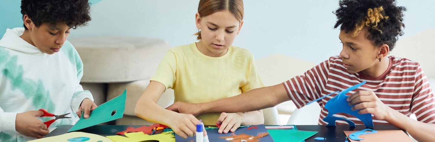 3 children sitting at a table with craft paper and glue