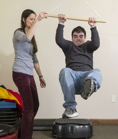 Person holding onto a swinging bar above their head while lifting their feet in the air. Therapist holding one end of the bar