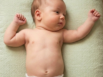 A caucasian appearing baby wearing only a white disposable diaper lies on a green textured cushion and looks to the left, his left arm is extended out to the same side and his right arm is bent in a "fencers position" demonstrating Asymmetrical Tonic Neck Reflex.